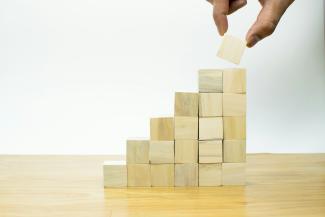 A person placing a piece of wood into a pyramid by Imagine Buddy courtesy of Unsplash.