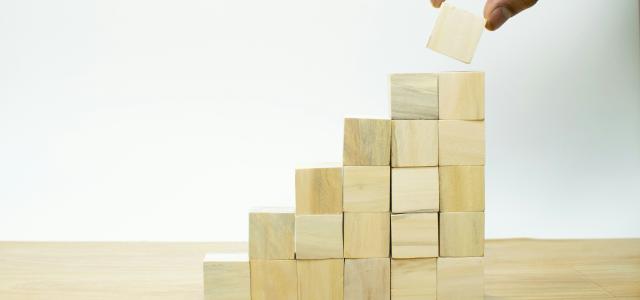 A person placing a piece of wood into a pyramid by Imagine Buddy courtesy of Unsplash.